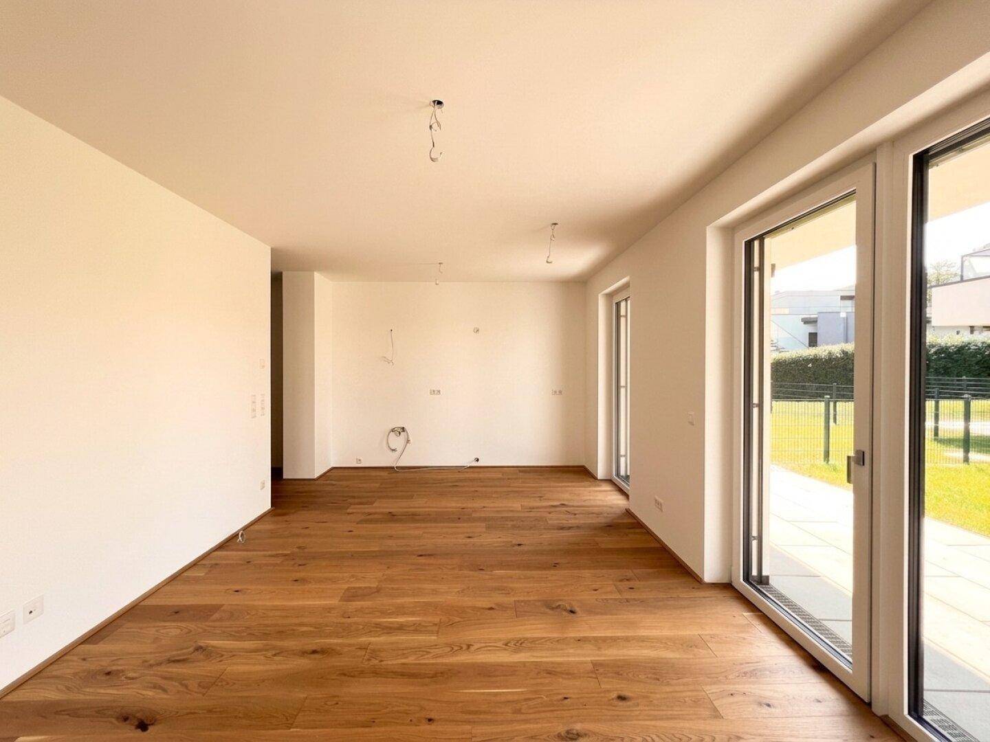 Heller, leerer Raum mit Holzboden und großen Schiebetüren, die zum Gartenbereich führen.