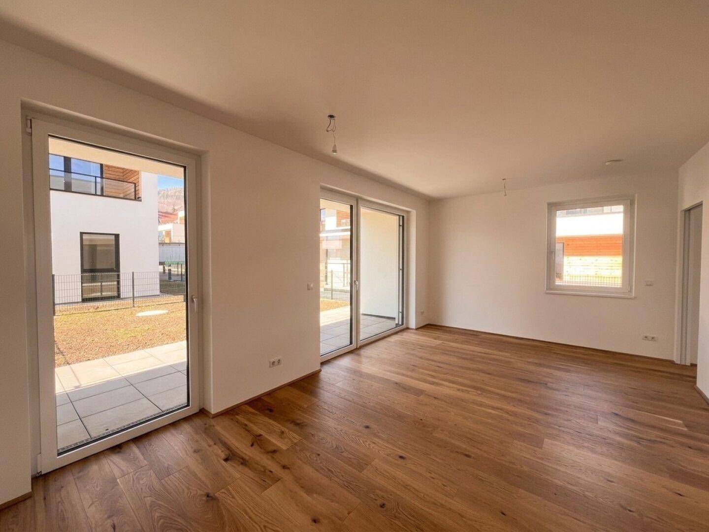 Geräumiger, heller Wohnbereich mit Holzboden und direktem Zugang zu einer Außenterrasse.