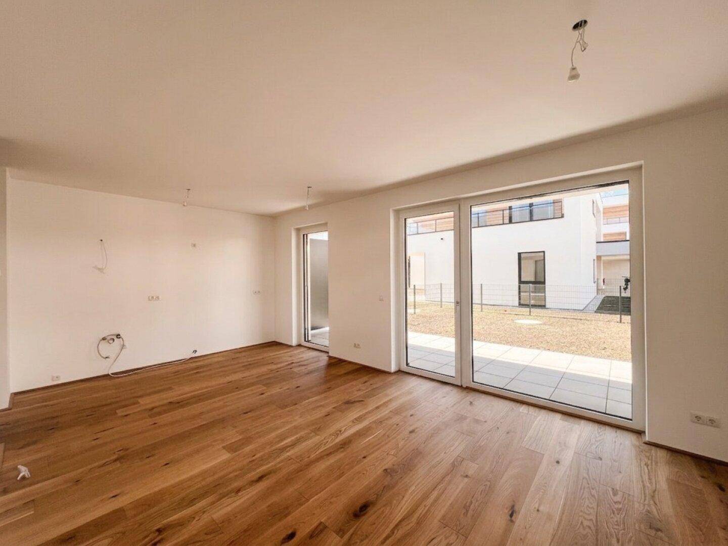 Lichtdurchfluteter Raum mit elegantem Holzboden und breiten Glasfronten zum Außenbereich.
