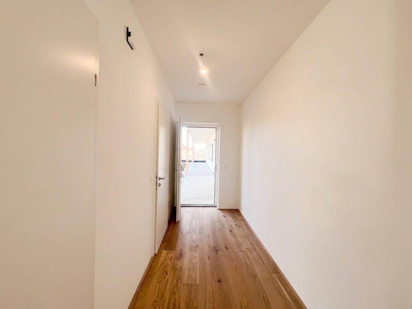 Heller Flur mit Holzboden und einer Tür, die zu einem hellen Außenbereich führt.