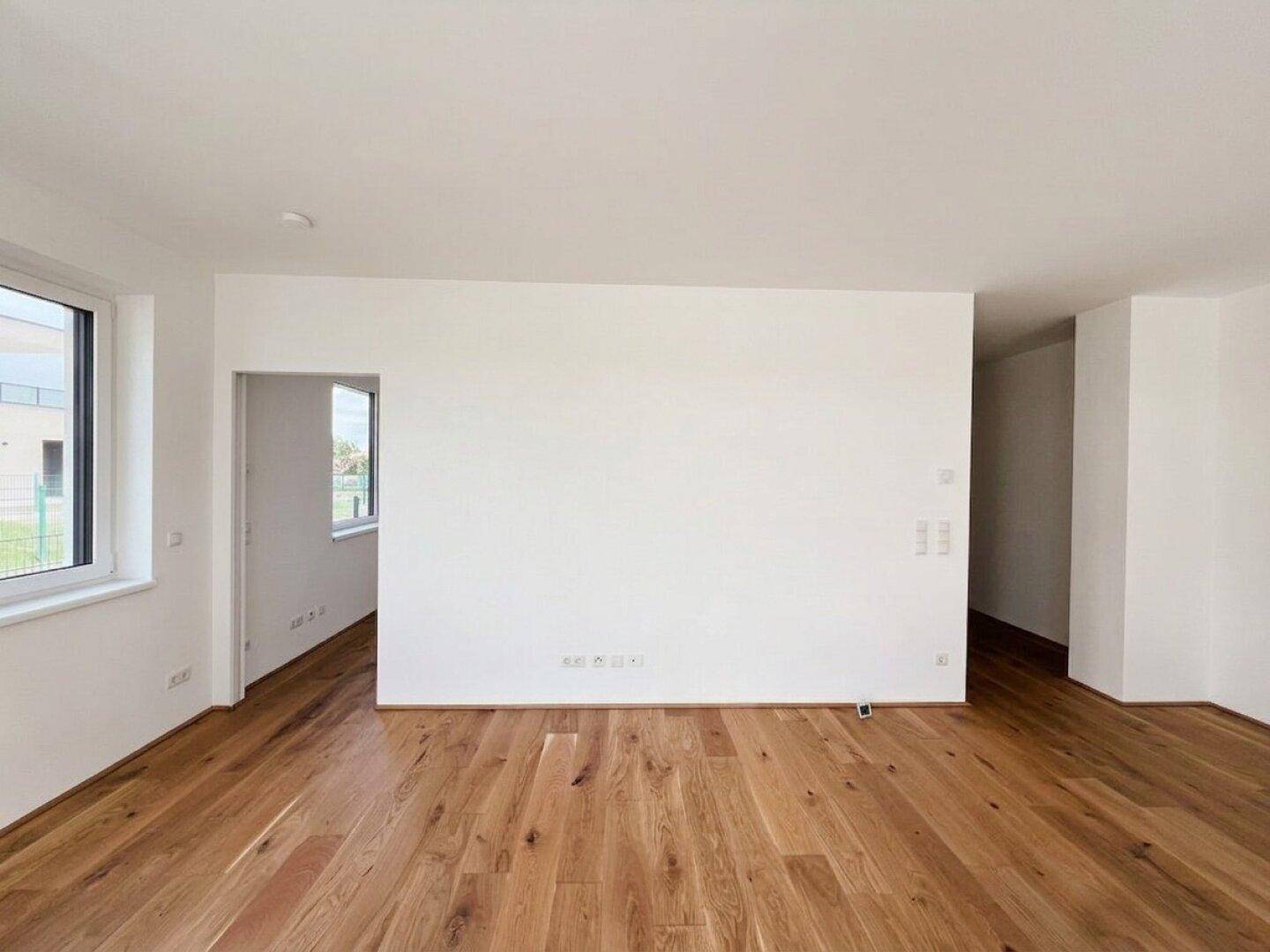 Offener Wohnbereich mit Holzboden und Fenstern, die den Raum mit Licht füllen.