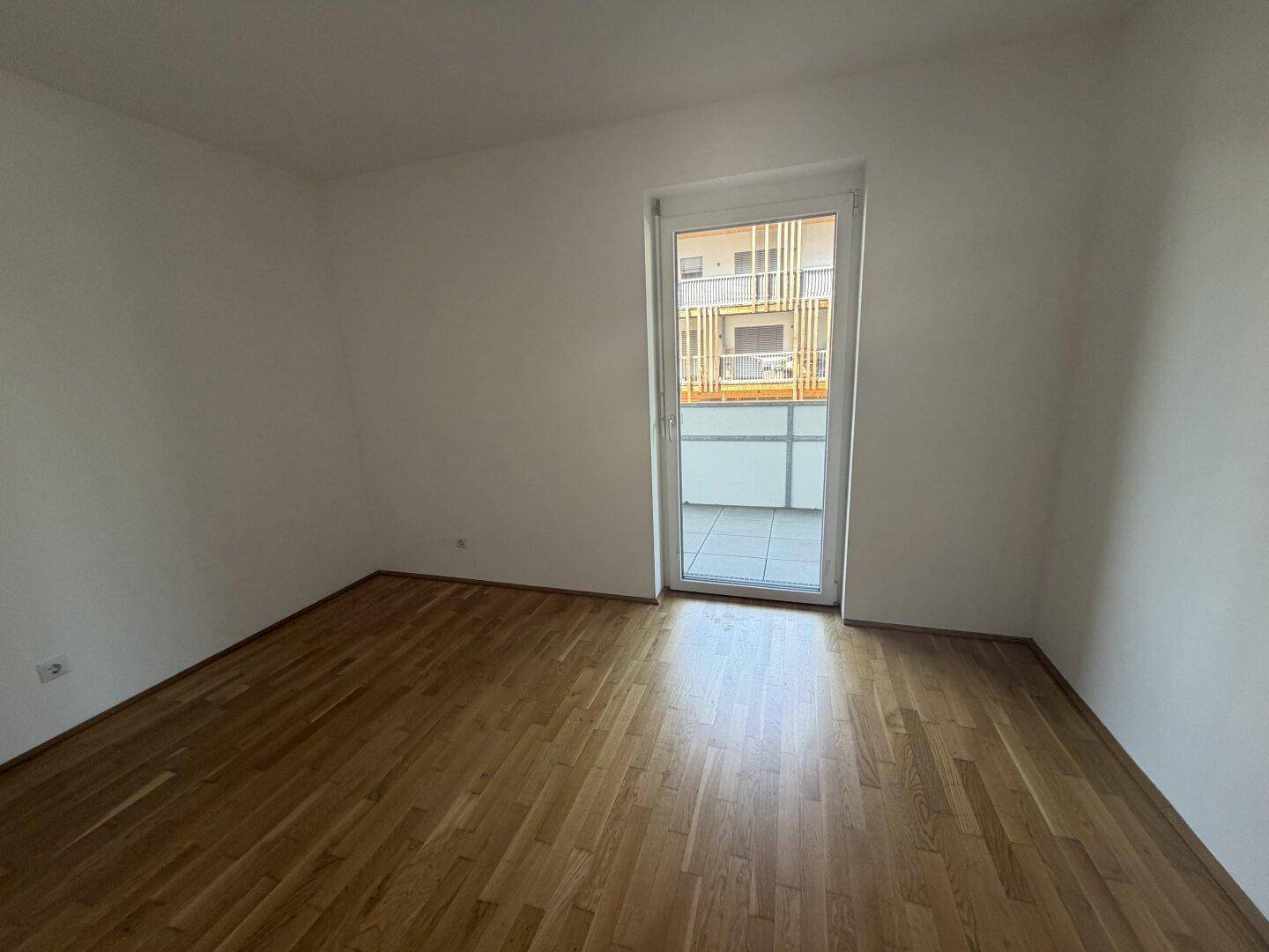 Helles Zimmer mit Parkettboden und direktem Zugang zum Balkon, ideal als Schlafzimmer oder Büro.