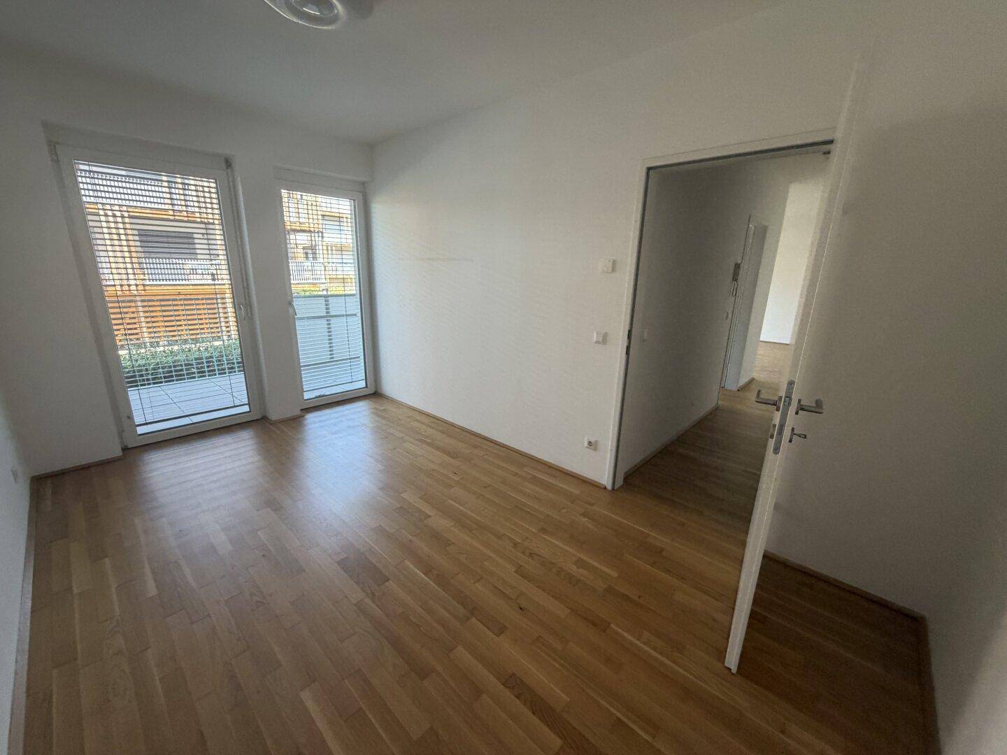 Geräumiges Zimmer mit Holzparkett und großen Fenstern, die viel Tageslicht hereinlassen.