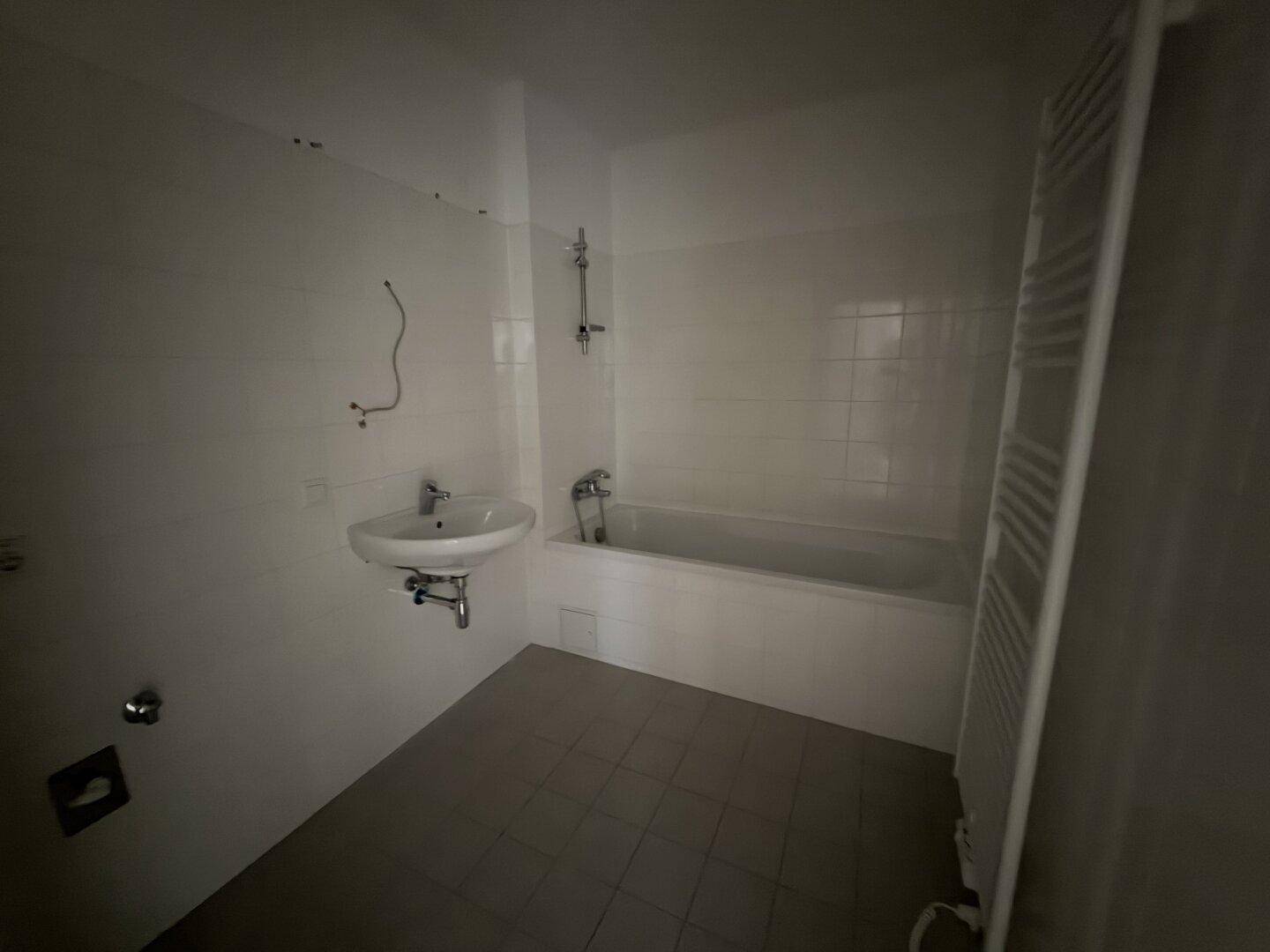 Badezimmer mit Badewanne, Waschbecken, weißen Fliesen und einem beheizten Handtuchhalter.