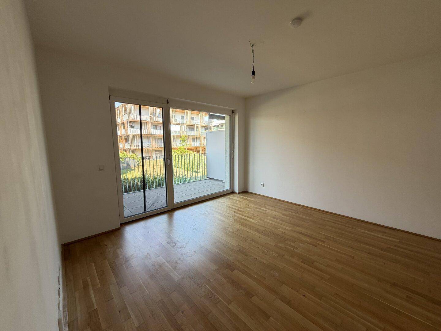 Geräumiges Wohnzimmer mit hellem Parkettboden und direktem Zugang zum Außenbereich.