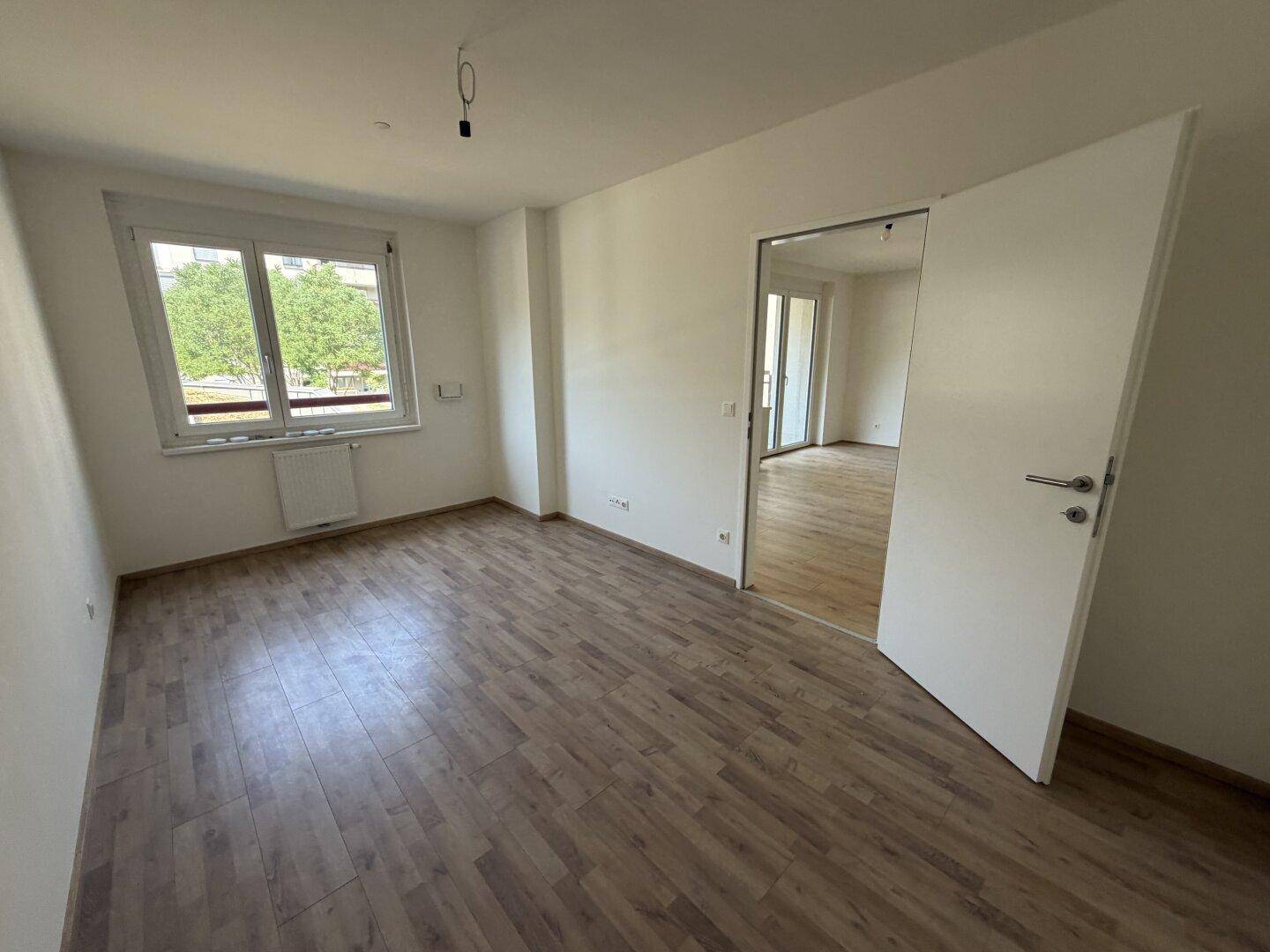 Helles Zimmer mit Holzboden und großem Fenster, das viel Tageslicht hereinlässt.