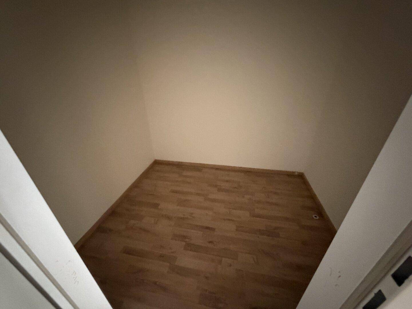 Kleiner, leerer Raum mit hellem Holzboden und beigen Wänden, vielseitig nutzbar.