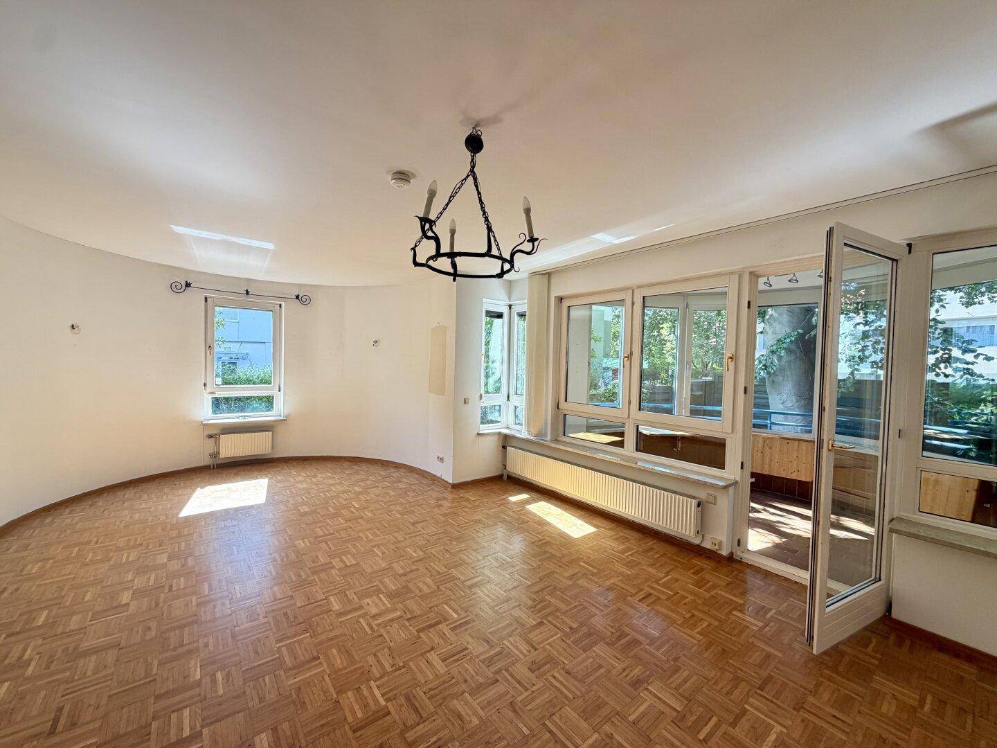Helles Wohnzimmer mit Parkettboden, geschwungener Wand und Zugang zu einem Wintergarten.