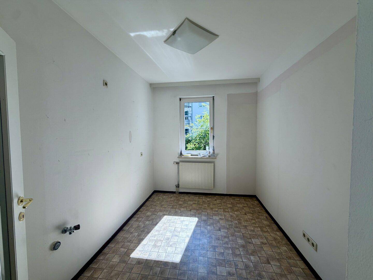 Kleiner Raum mit Linoleumboden, Fenster und Anschlüssen für eine mögliche Küchenzeile.