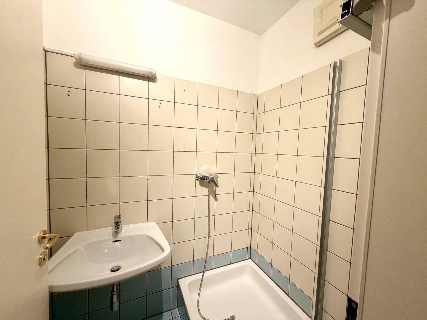 Badezimmer mit Dusche, Waschbecken und hellblauen Fliesen im 80er-Jahre-Stil.