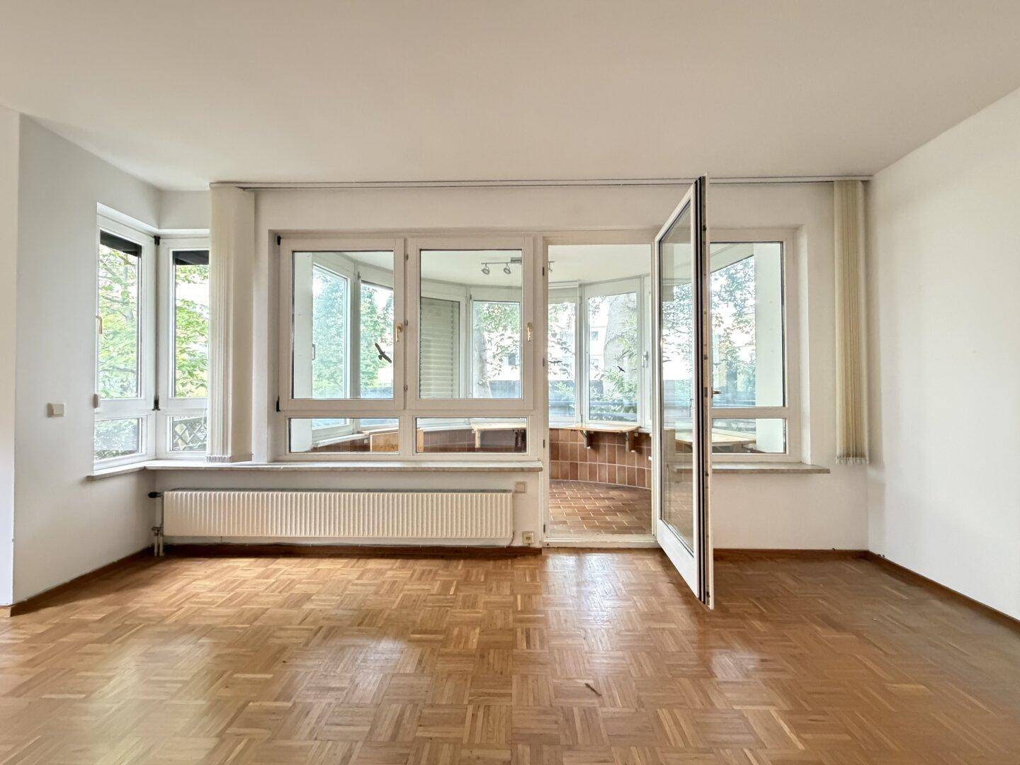 Helles Wohnzimmer mit Parkettboden und offenem Zugang zum verglasten Wintergarten.