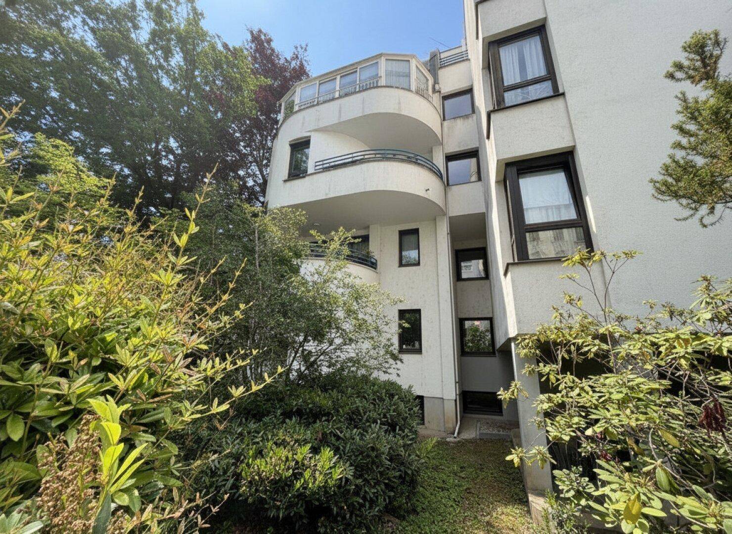 Moderne Gebäudefassade mit geschwungenen Balkonen und viel Grün in der Umgebung.