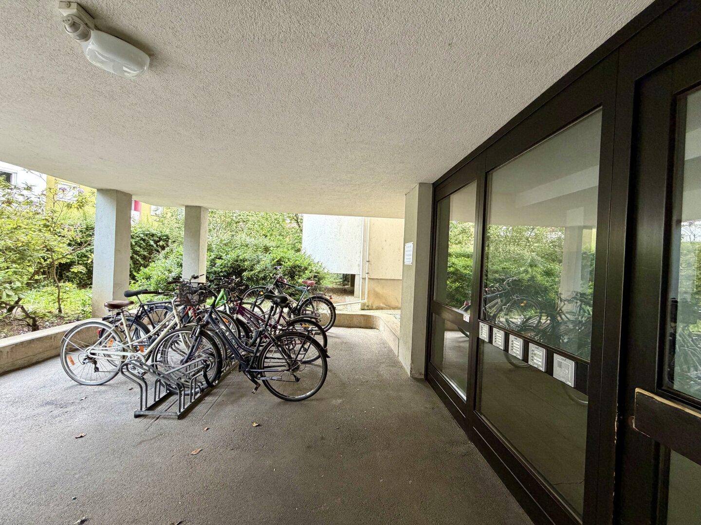 Eingangsbereich des Gebäudes mit Fahrradständern und viel Grün im Hintergrund.