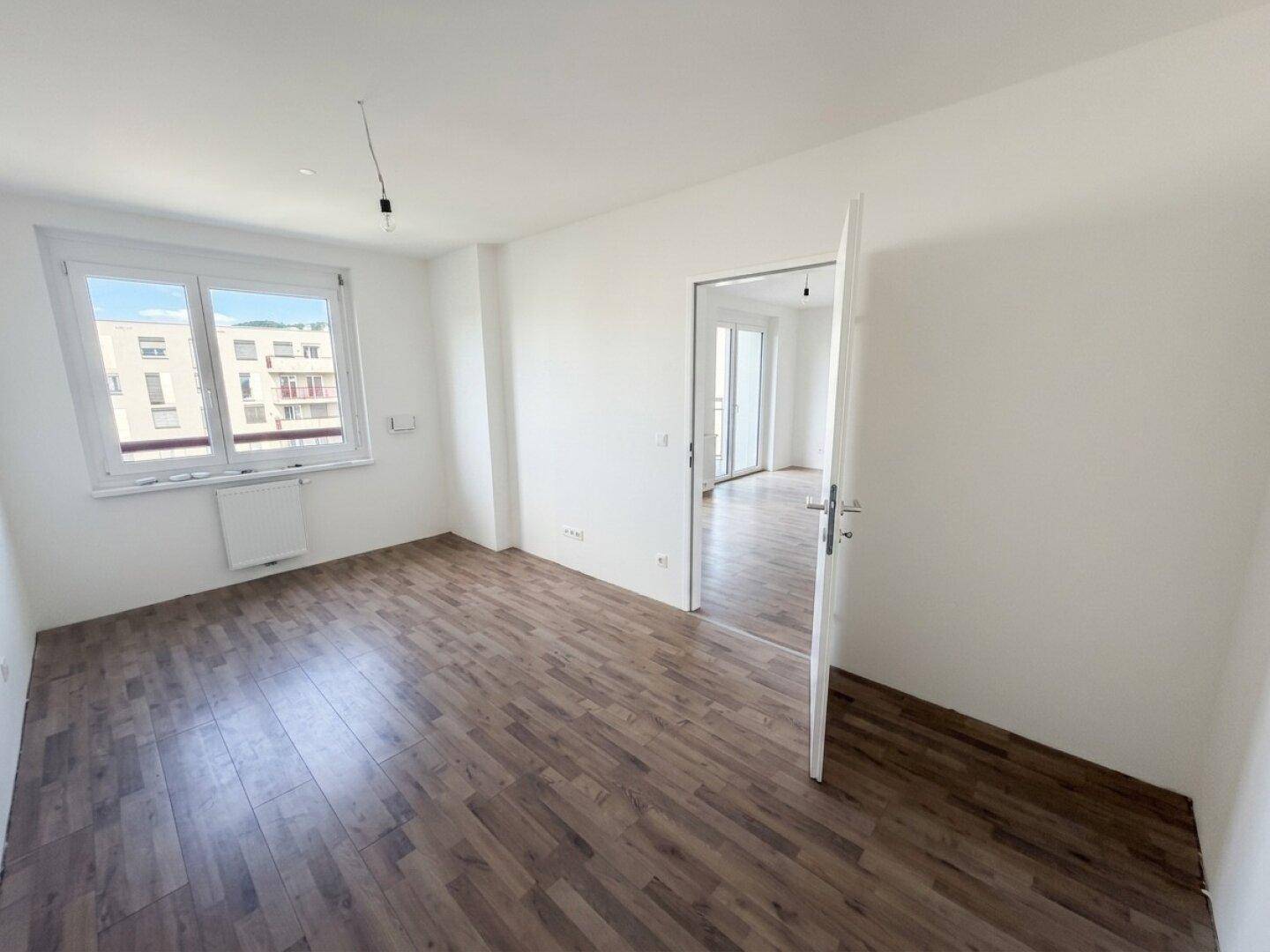 Leeres Zimmer mit Laminatboden und einem Fenster, das einen Blick auf die Umgebung bietet.