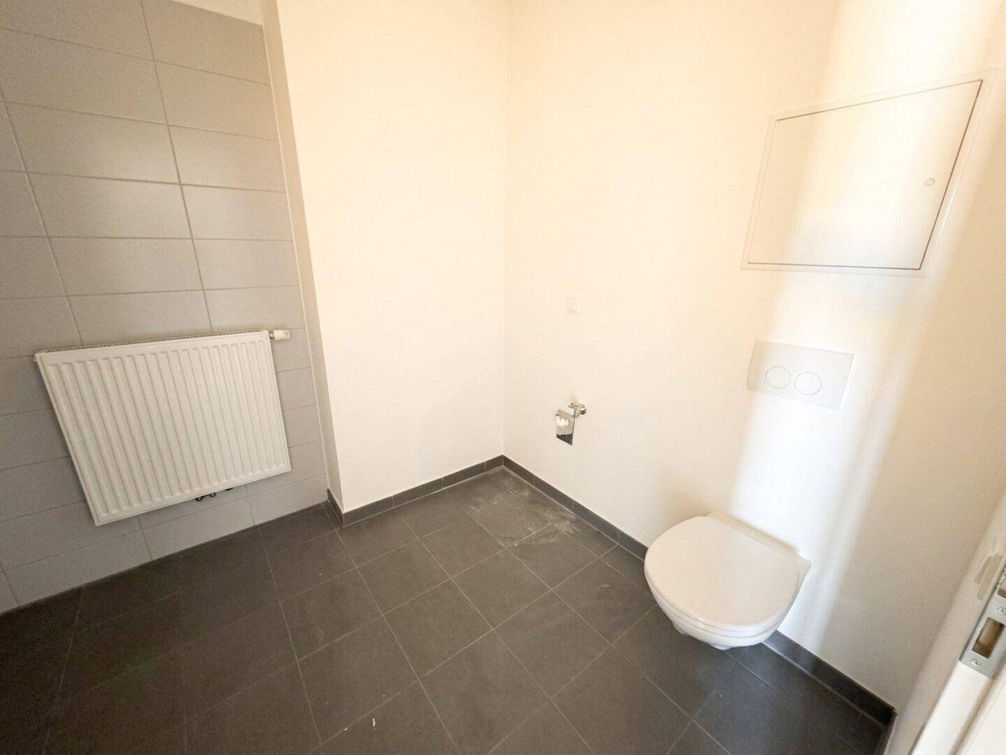 Separates WC mit Wand-WC und grauen Bodenfliesen, sauber und funktional gestaltet.