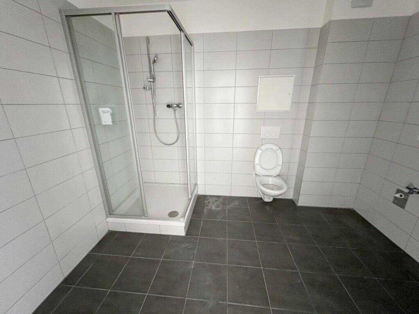 Modernes Badezimmer mit grauen Fliesen, einer Duschkabine und wandmontiertem WC.