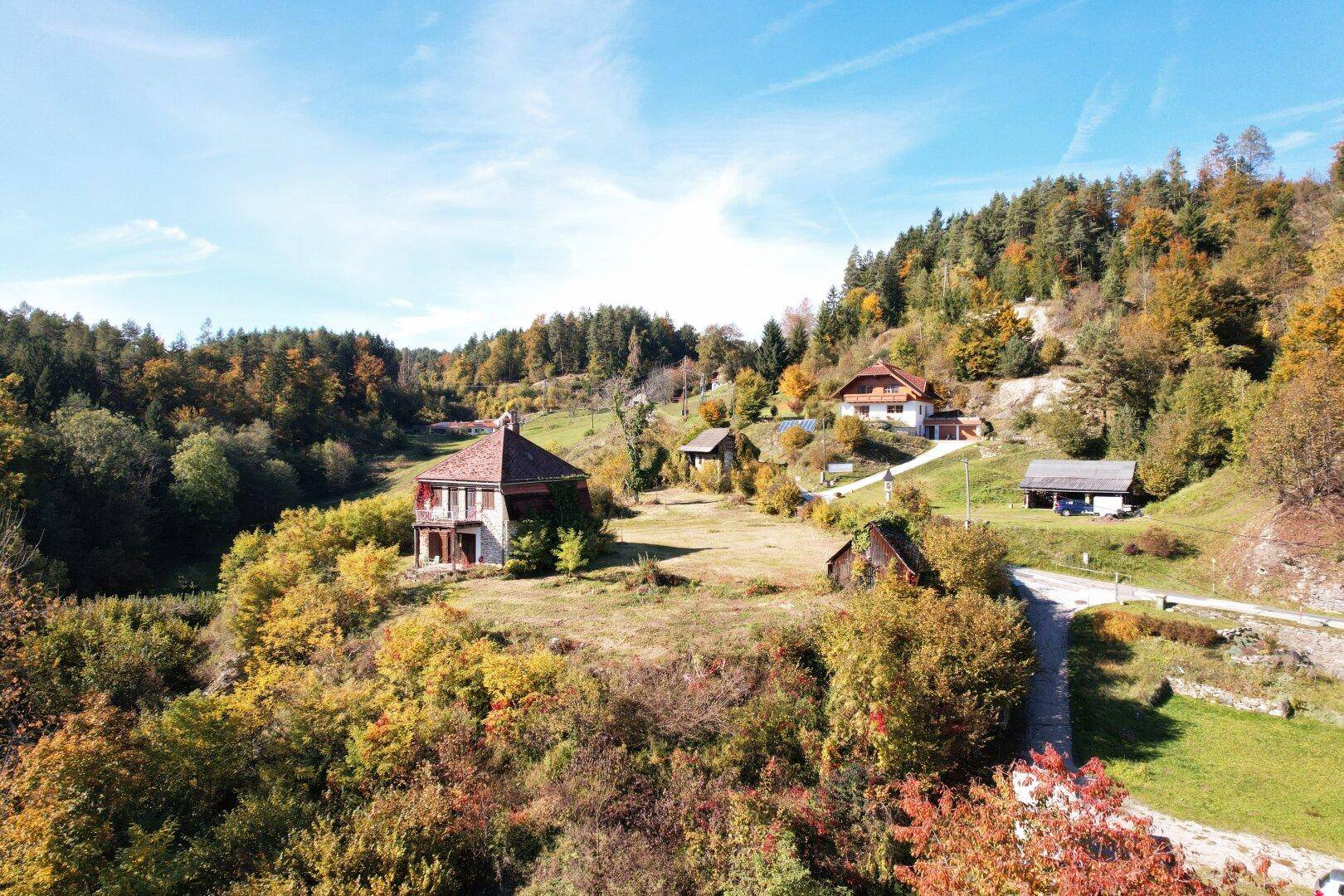 Panoramablick auf ein Anwesen mit mehreren Gebäuden, umgeben von üppiger Natur und Hügeln.