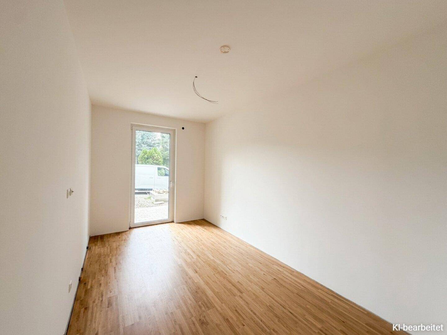Leeres Zimmer mit Holzboden und einer Tür, die nach draußen führt, ideal für ein Schlafzimmer.