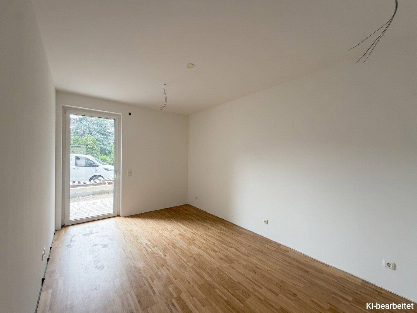 Unmöbliertes Zimmer mit Holzboden und einer Glastür, die Zugang zum Außenbereich bietet.