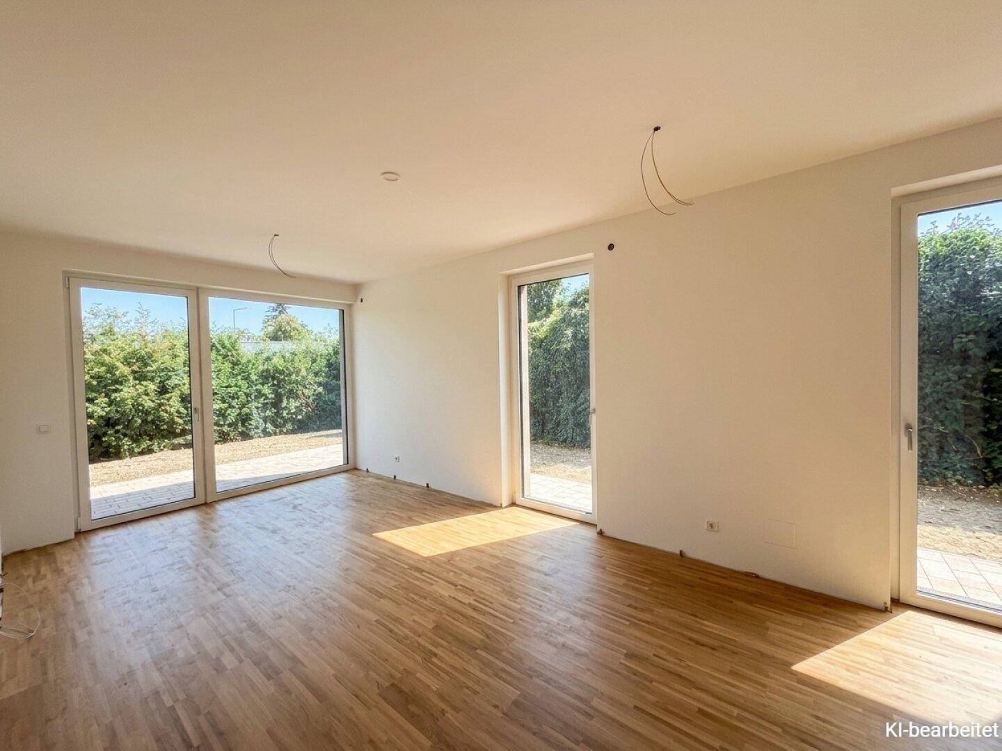 Heller, leerer Raum mit Holzboden und großen Fenstern, die viel Tageslicht hereinlassen.