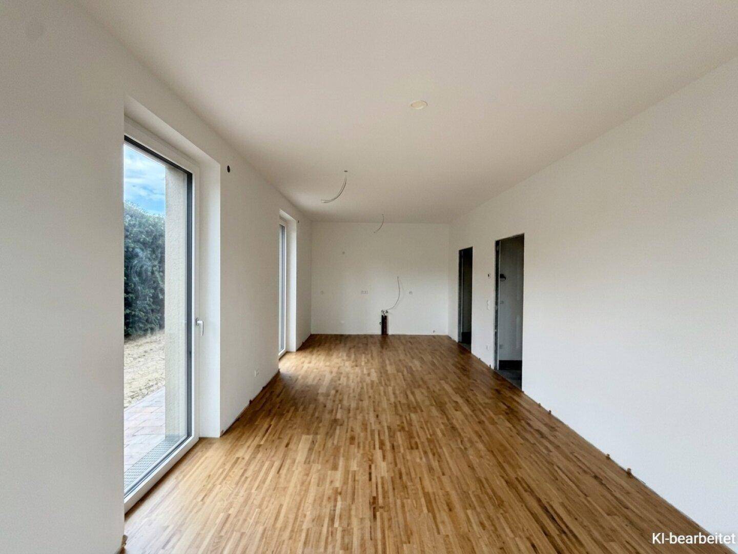Langer, heller Raum mit Holzboden und einer großen Fensterfront, die den Blick ins Grüne freigibt.