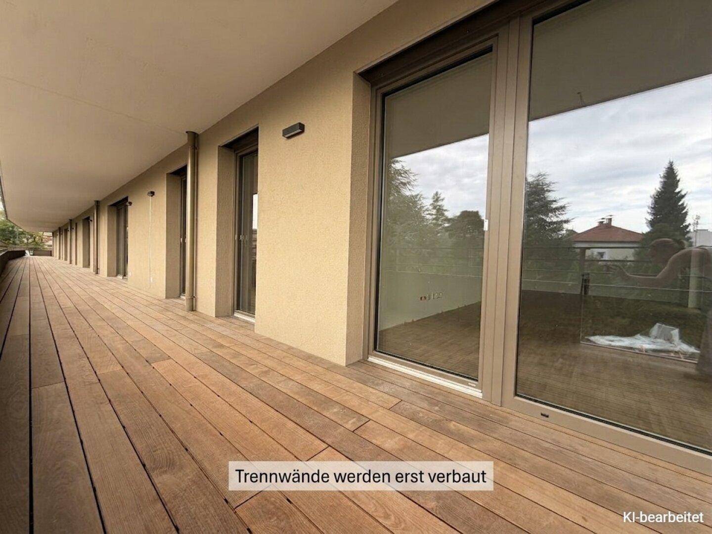 Langer Balkon mit Holzboden und großen Glasfronten, die Zugang zu den Innenräumen bieten.