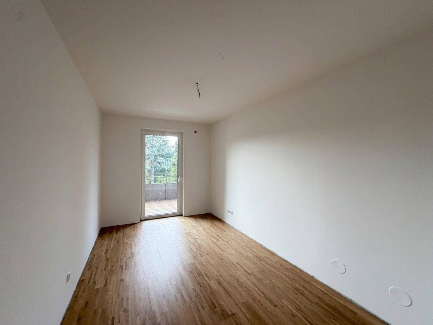 Helles, unmöbliertes Zimmer mit Holzboden und Balkonzugang, ideal als Schlafzimmer.