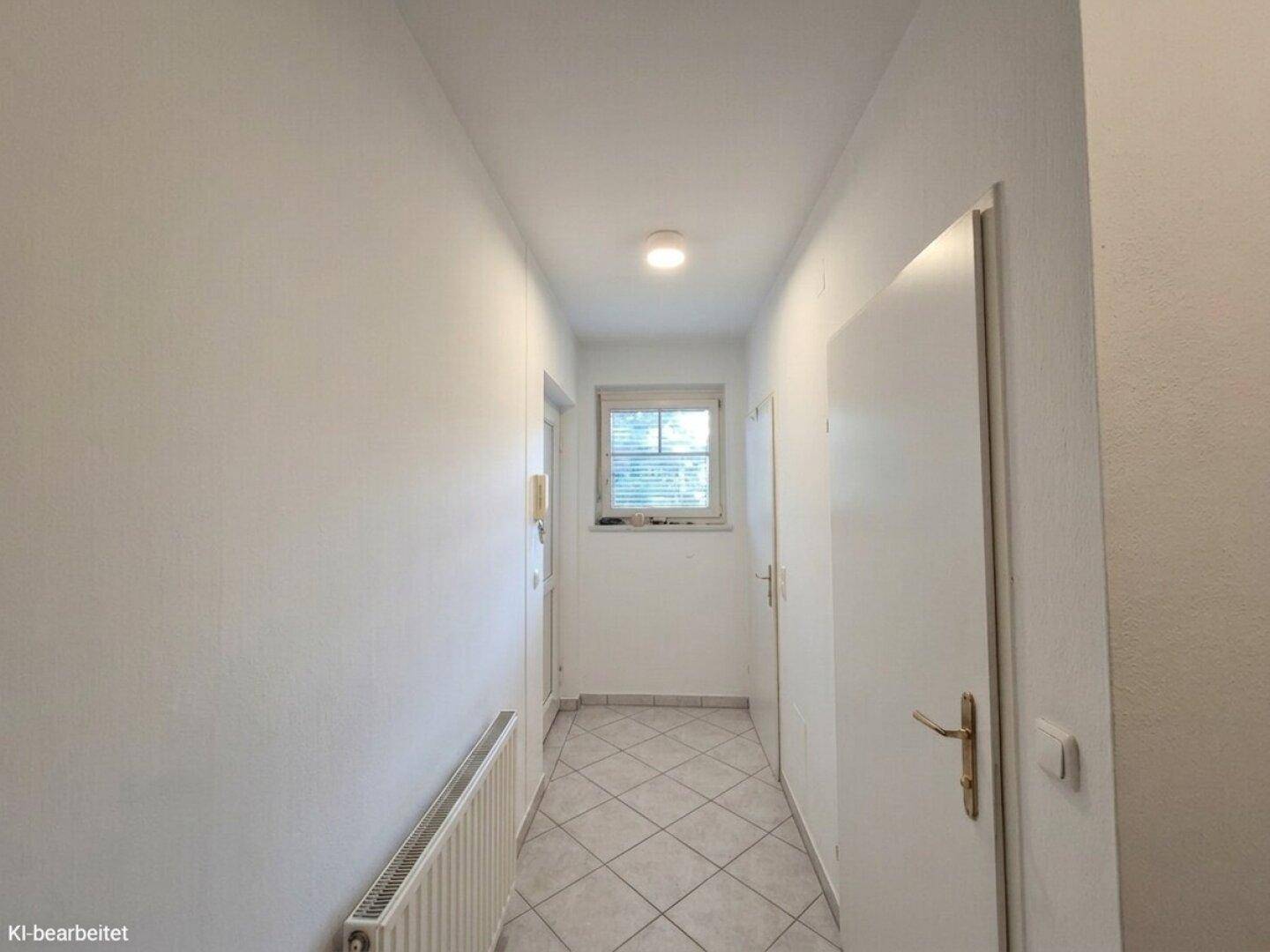 Heller Flur mit Fliesenboden und einem Fenster am Ende, das Tageslicht hereinlässt.