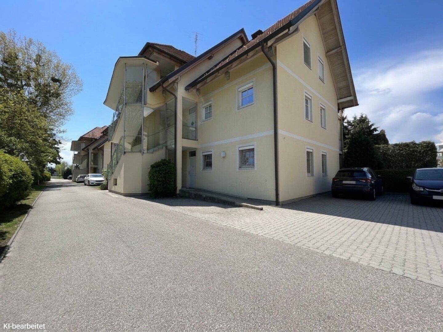 Außenansicht des Wohngebäudes mit heller Fassade, Zufahrt und Parkplätzen.