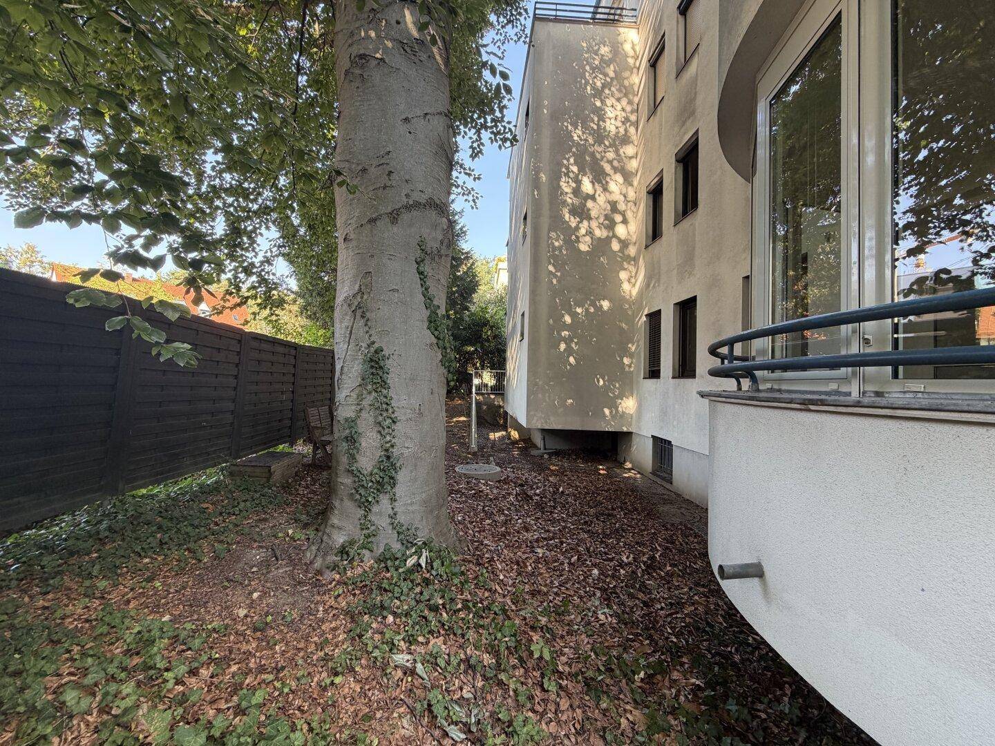 Seitenansicht des Gebäudes mit großem Baum, Holzzaun und einem kleinen Balkon an der Fassade.