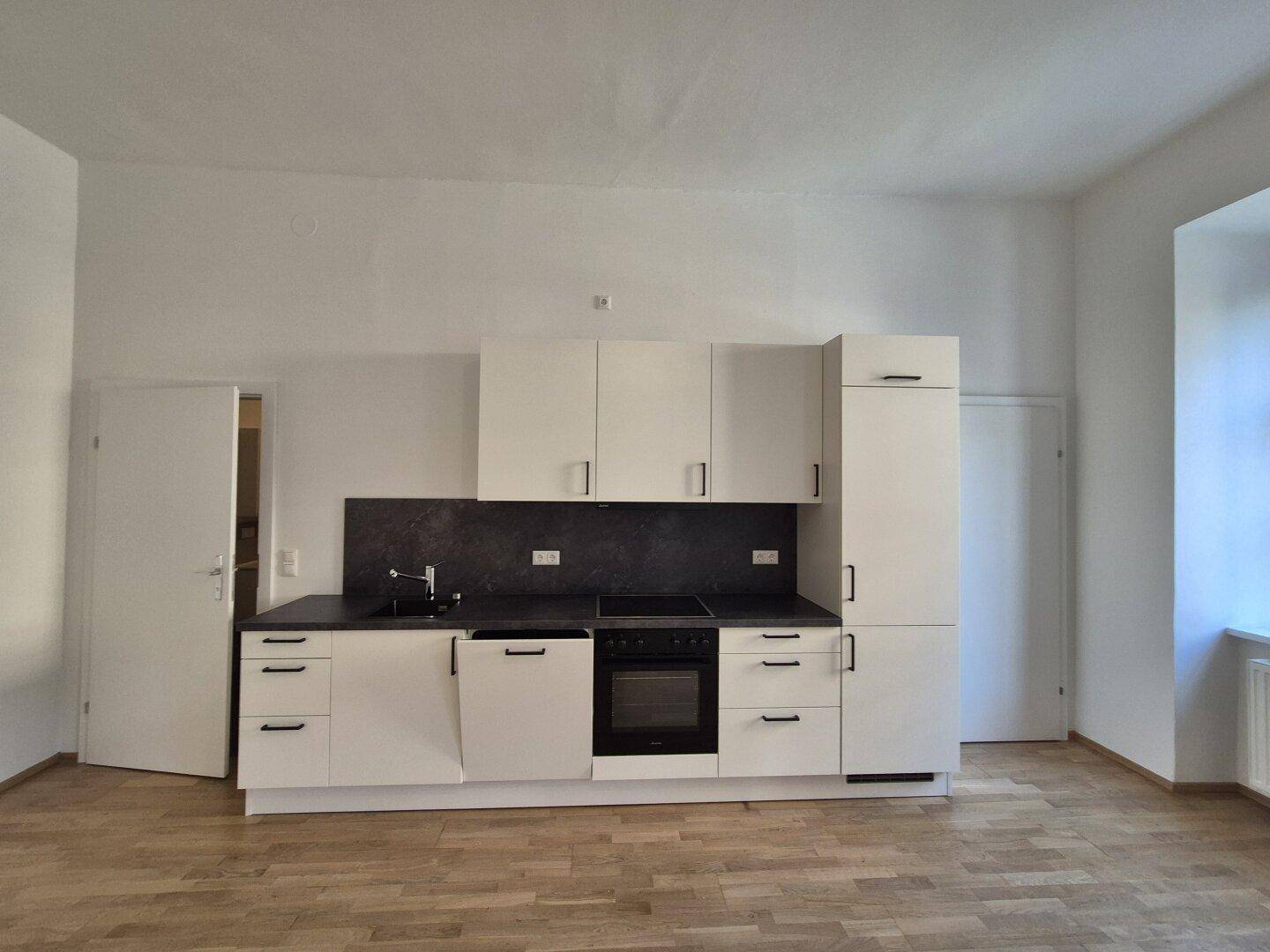 Moderne weiße Einbauküche mit dunkler Arbeitsplatte und integrierten Geräten in einem hellen Raum.