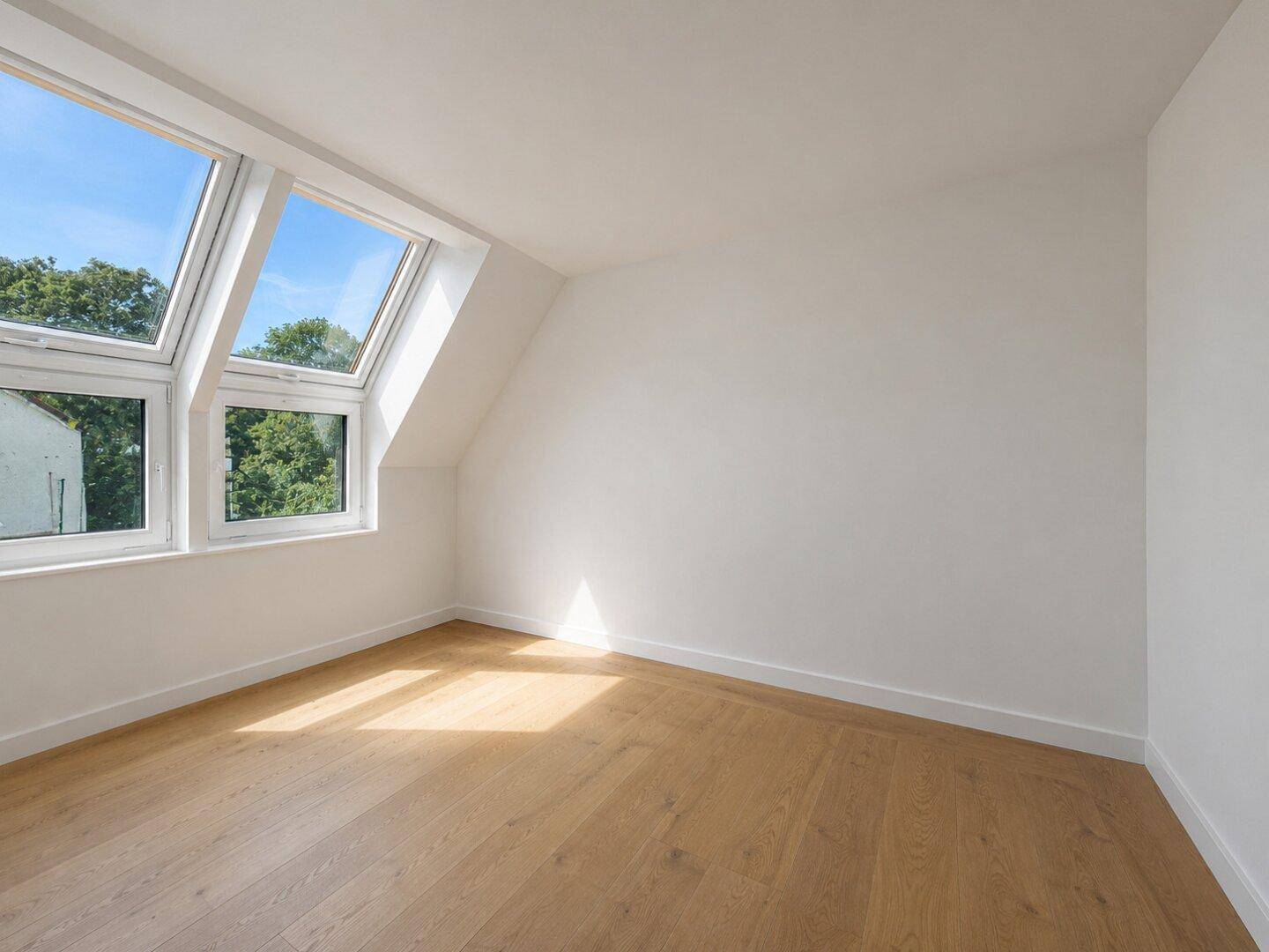 Leeres, helles Schlafzimmer im Dachgeschoss mit Holzboden und großen Dachfenstern.
