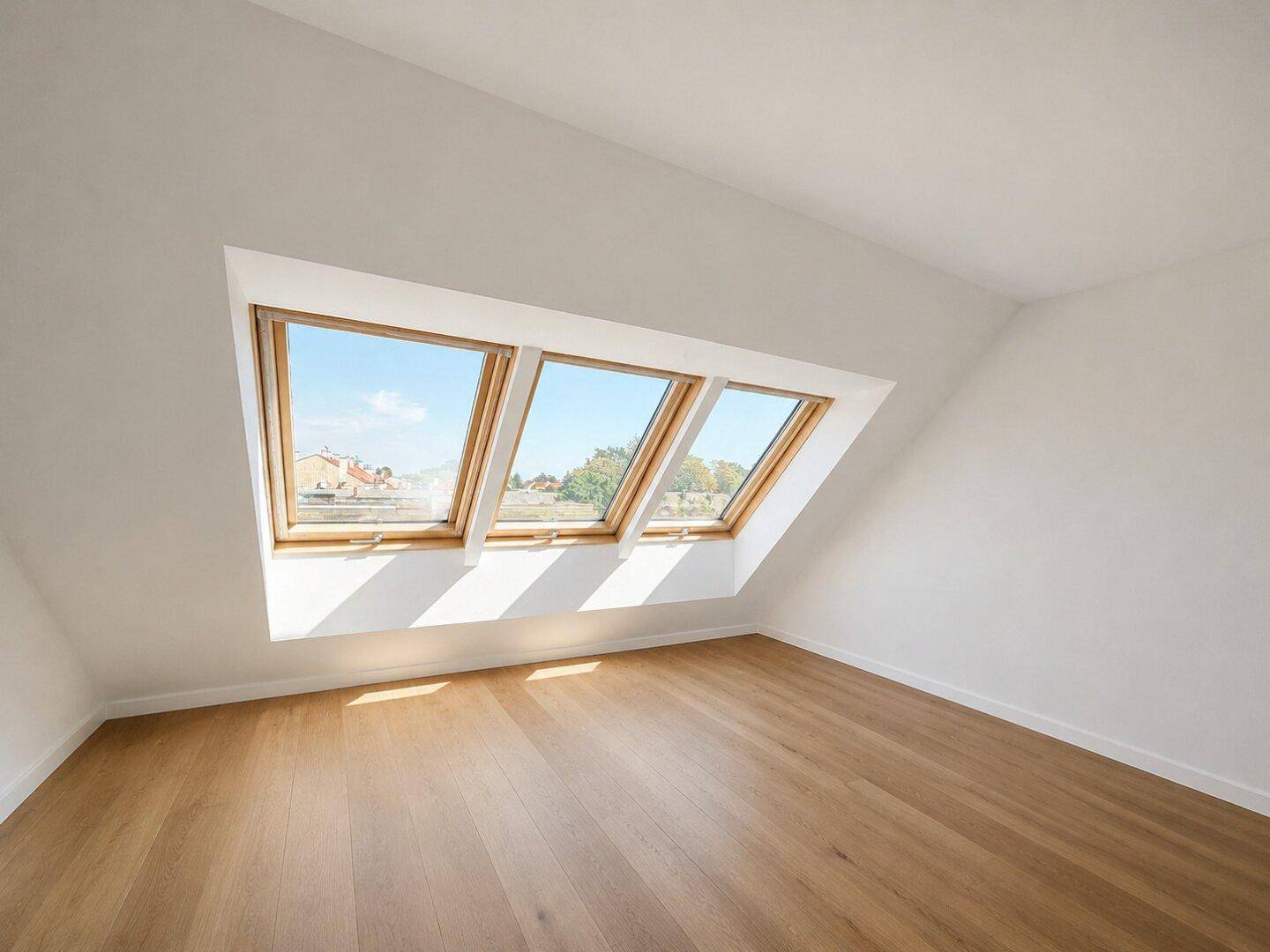 Leeres Schlafzimmer im Dachgeschoss mit Holzboden und drei großen Dachfenstern.