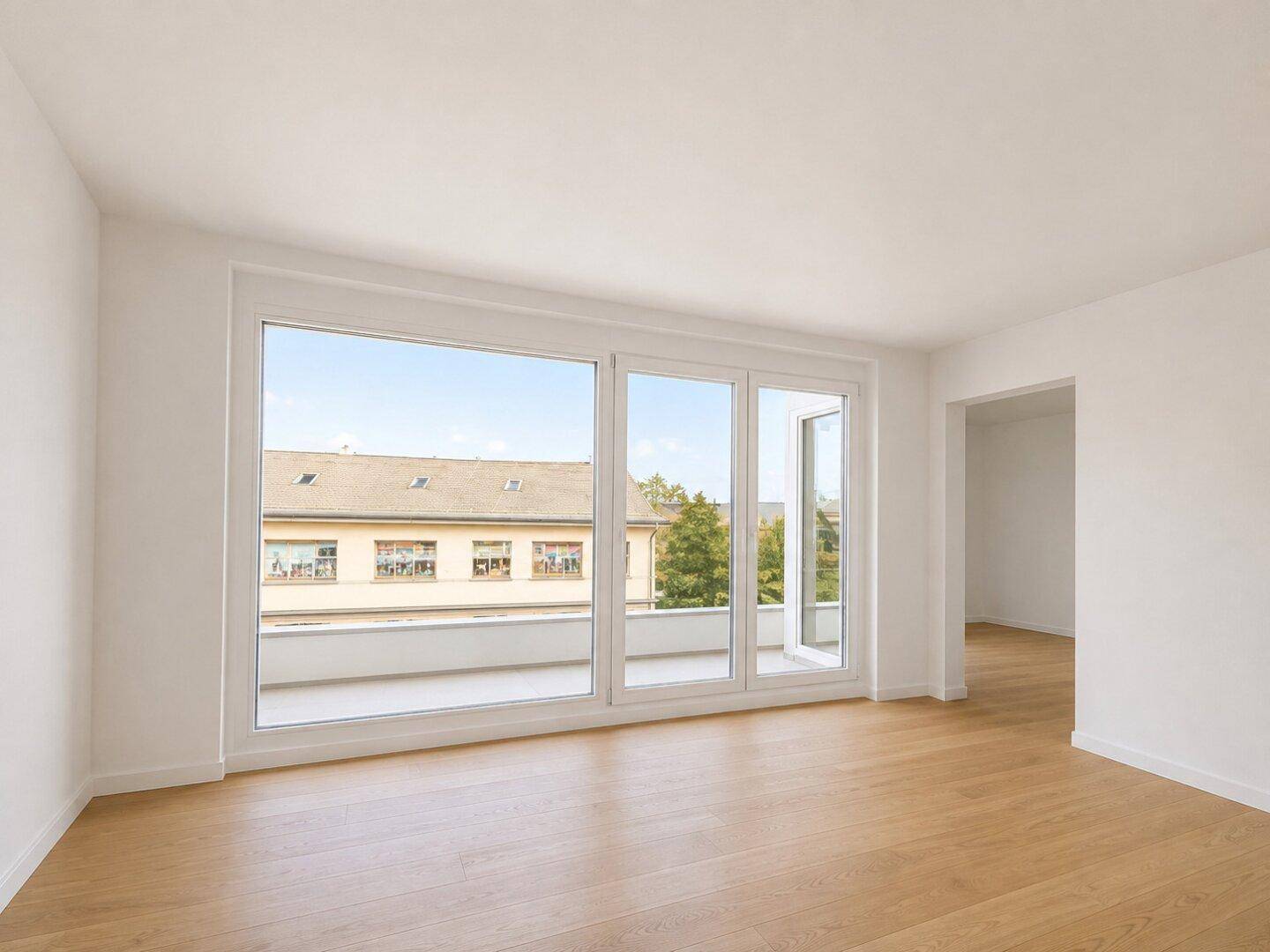 Geräumiger, leerer Wohnbereich mit großen Fenstern und Zugang zu einem Balkon.