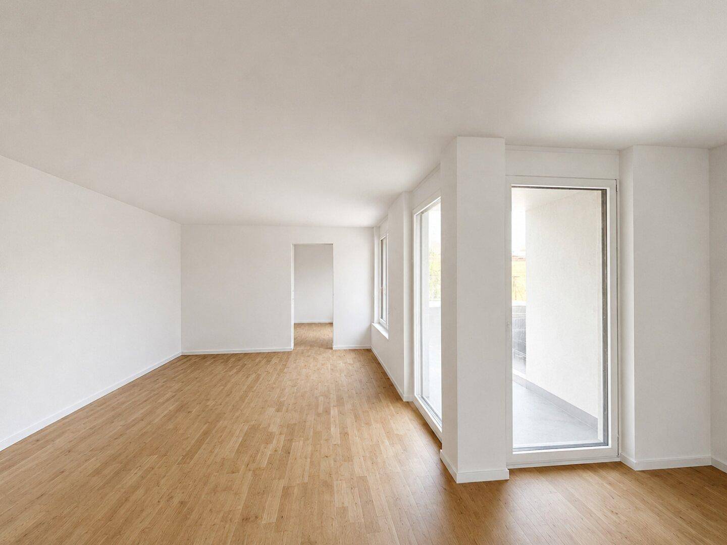 Geräumiges, leeres Zimmer mit Holzboden, großen Fenstern und Zugang zu einem Außenbereich.