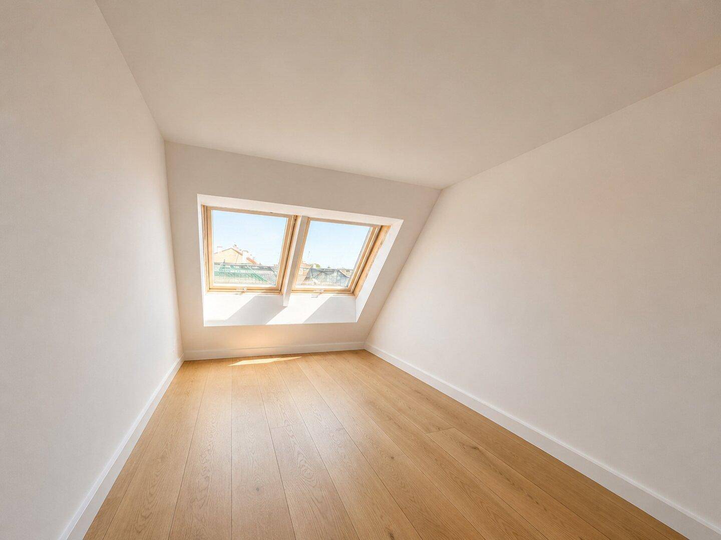 Helles, leeres Zimmer mit Dachschrägen und zwei großen Dachfenstern.
