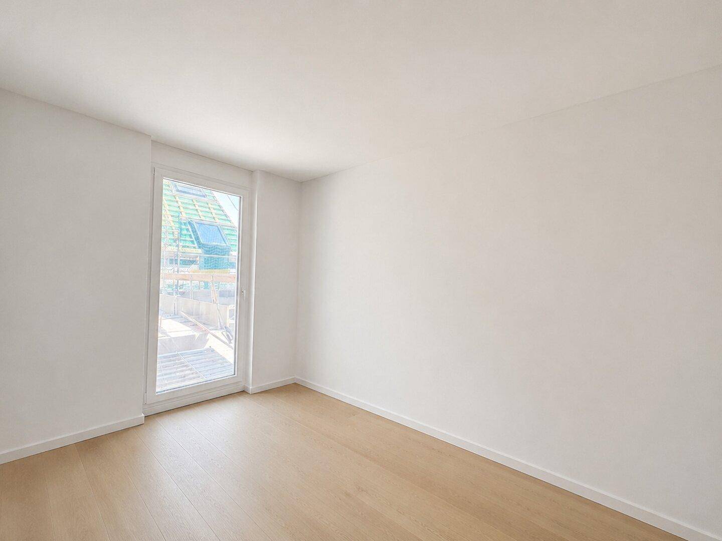 Leerer Raum mit Holzboden und Fenster, das viel Tageslicht hereinlässt.