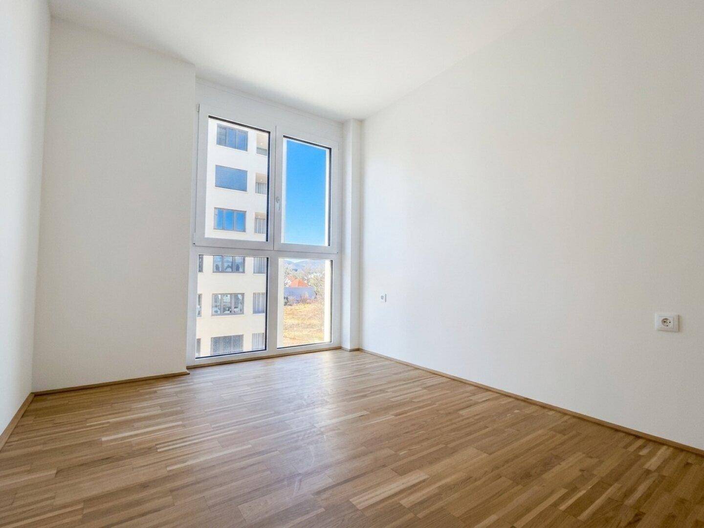 Helles Schlafzimmer mit Parkettboden und großem Fenster, das einen weiten Blick bietet.