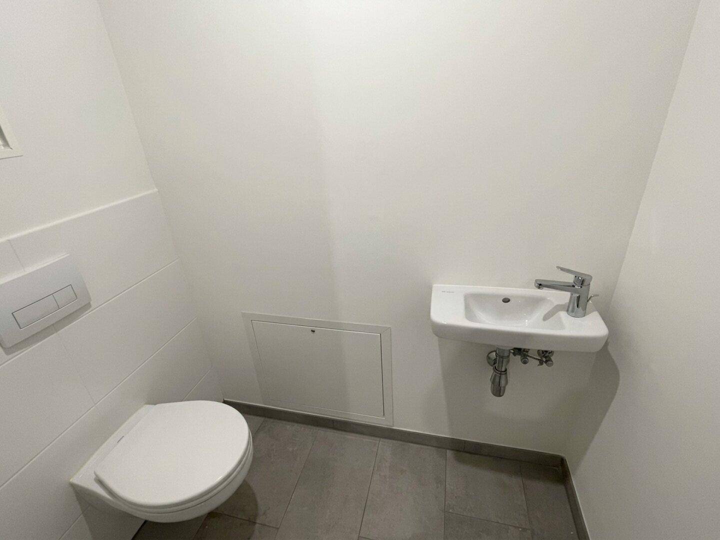 Modernes Gäste-WC mit wandhängender Toilette und kleinem Waschbecken, in schlichtem Design.