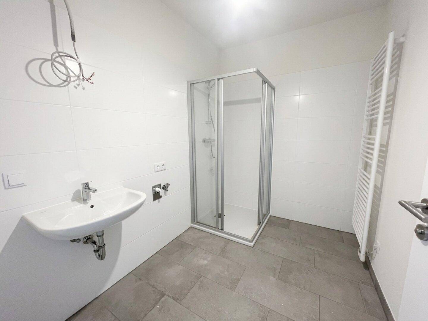 Helles Badezimmer mit Duschkabine, Waschbecken und beheiztem Handtuchhalter, modern gefliest.