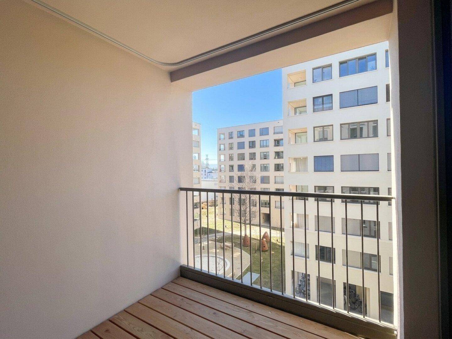 Balkon mit Holzboden und Blick auf den Innenhof und die umliegenden modernen Gebäude.