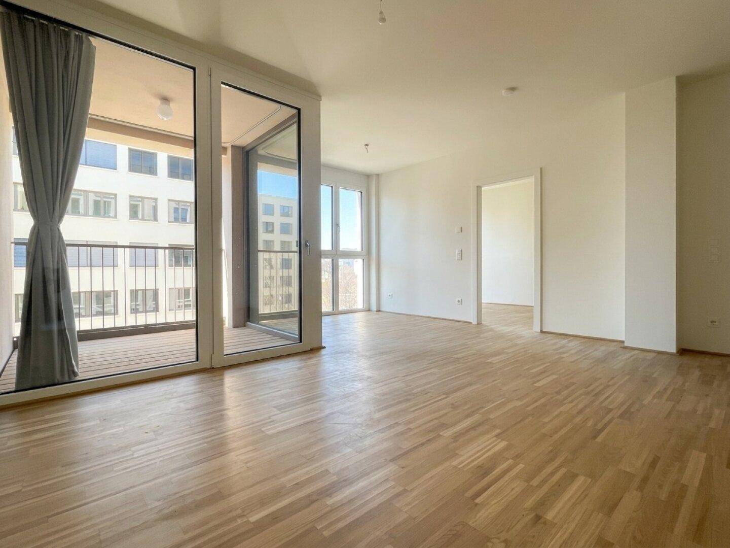 Lichtdurchfluteter Raum mit Holzboden und Zugang zu einem Balkon, bietet eine offene Gestaltungsmöglichkeit.