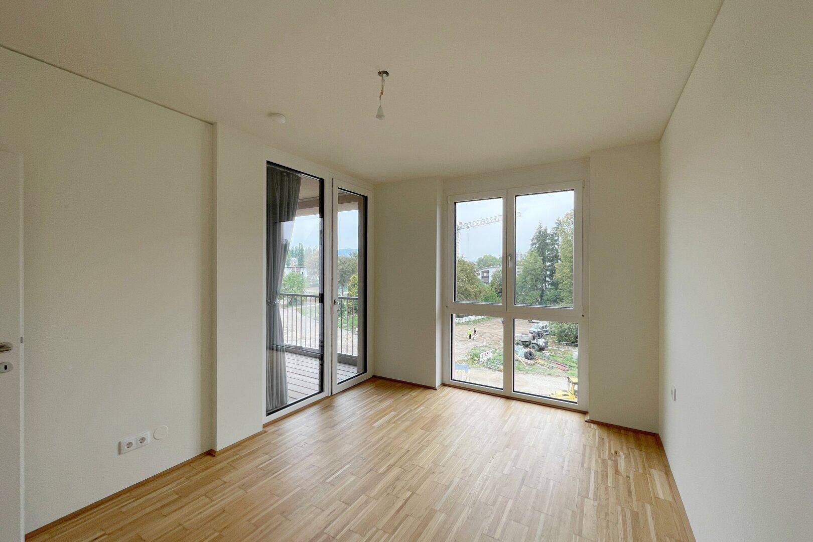 Helles Schlafzimmer mit Parkettboden und Zugang zu einem französischen Balkon mit Aussicht.
