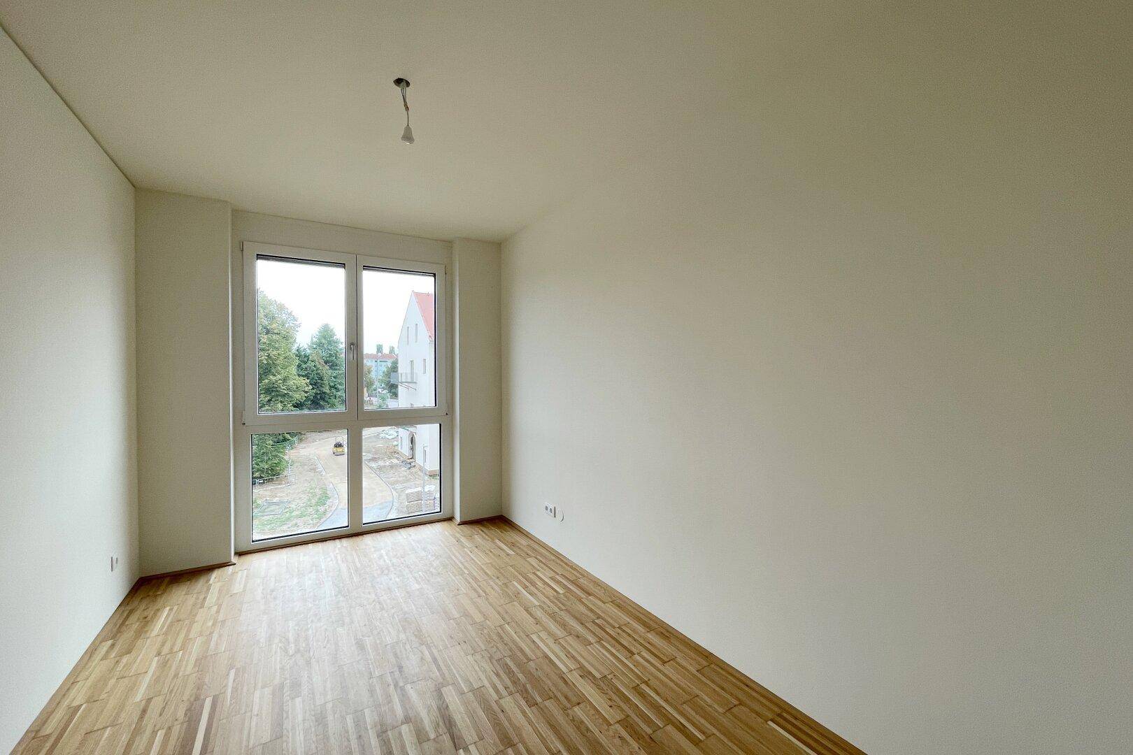 Geräumiges Zimmer mit Parkettboden und großem Fenster, das viel Tageslicht hereinlässt.