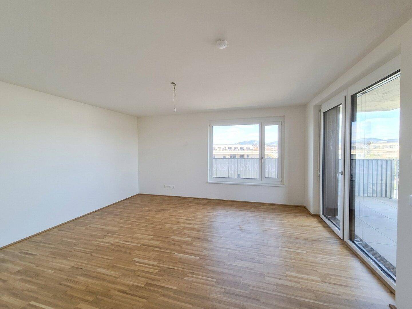 Helles, leeres Zimmer mit Parkettboden und Zugang zu einem Balkon, bereit zur individuellen Gestaltung.
