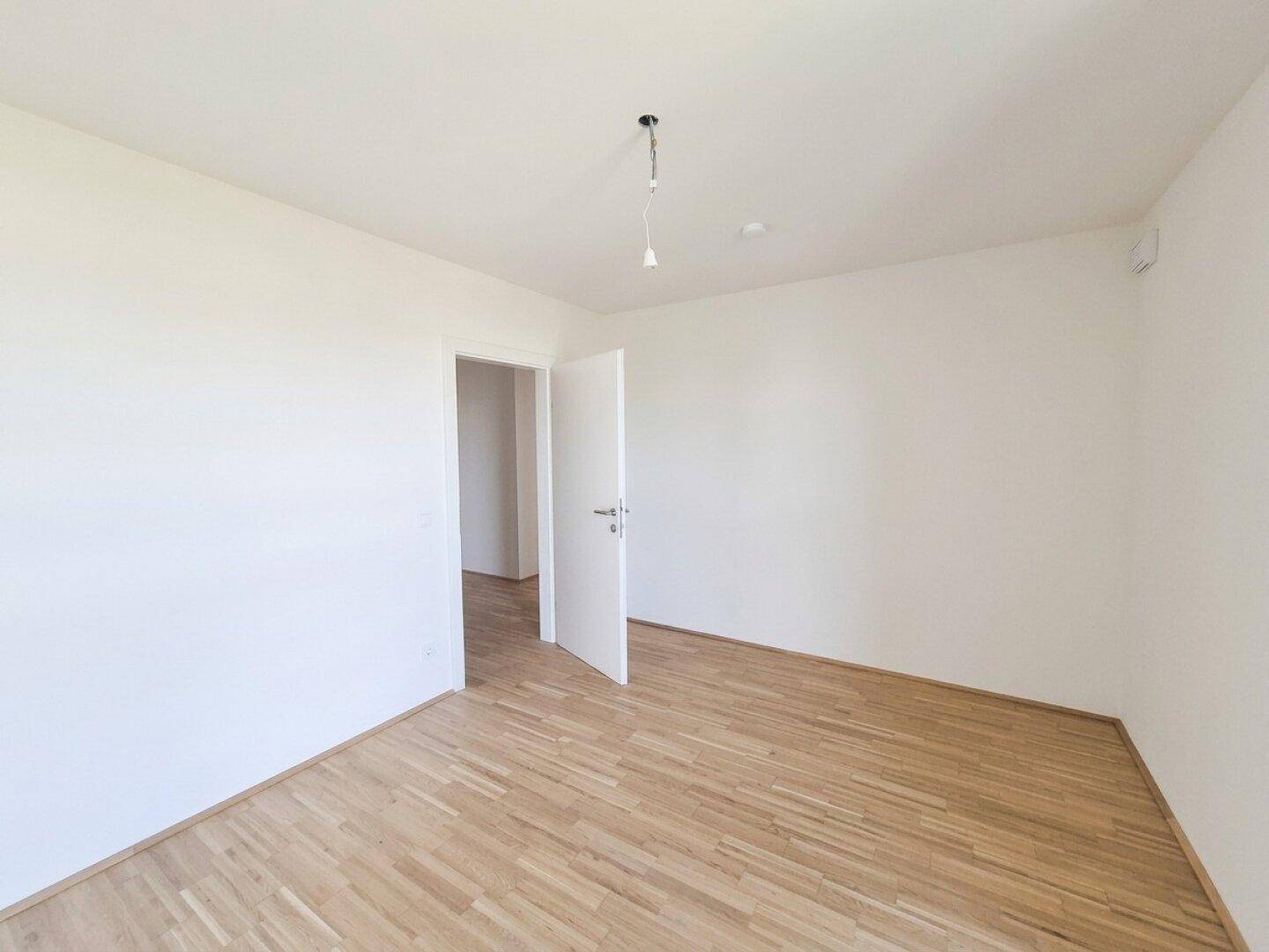 Unmöbliertes Schlafzimmer mit Parkettboden und einer Tür, die zu einem weiteren Raum führt.