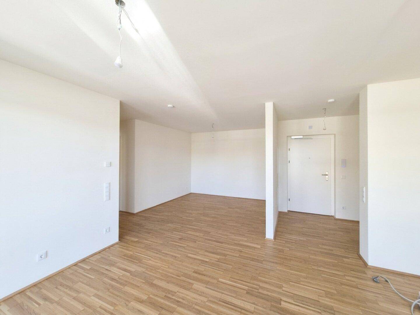 Heller Eingangsbereich mit Parkettboden und weiß gestrichenen Wänden in einem modernen Neubau.