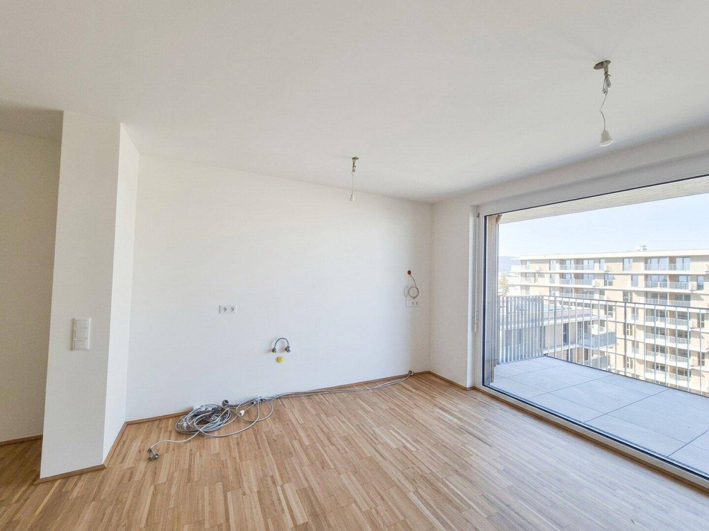 Unmöblierter Wohnraum mit Parkettboden, großen Fenstern und direktem Zugang zur Terrasse.