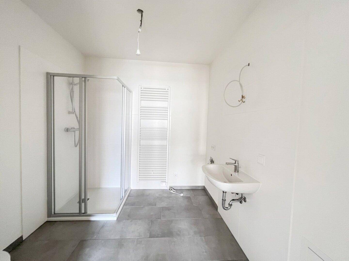 Modernes Badezimmer mit Duschkabine, Waschbecken und beheiztem Handtuchhalter in neutralen Farben.