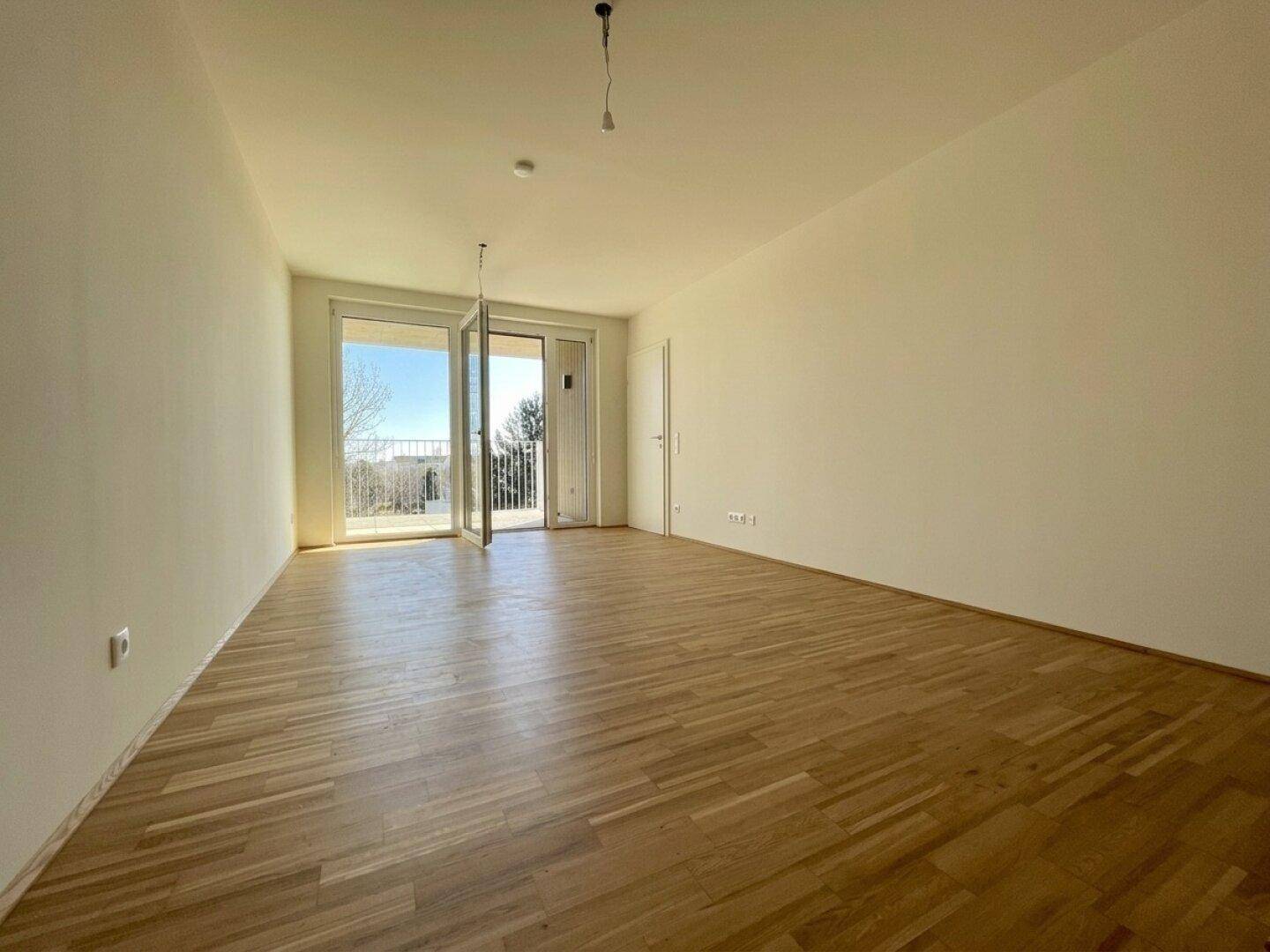 Heller Raum mit Parkettboden und Zugang zu einem Balkon mit Weitblick ins Grüne.